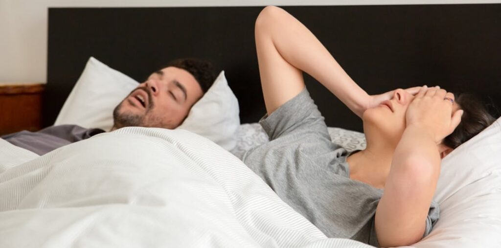 A girl is trying to sleep while a man snores, and she wonders if sleep apnea is the issue.