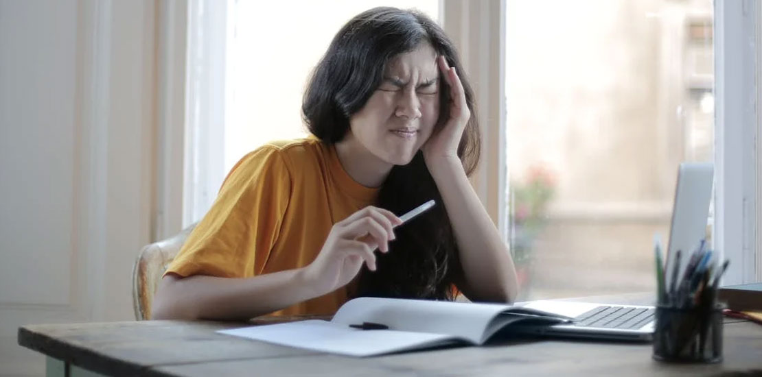 zena koja sedi za stolom i drzi se za glavu