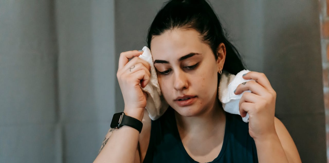 A woman wiping sweat from her face with a towel, showing signs of discomfort due to excessive sweating