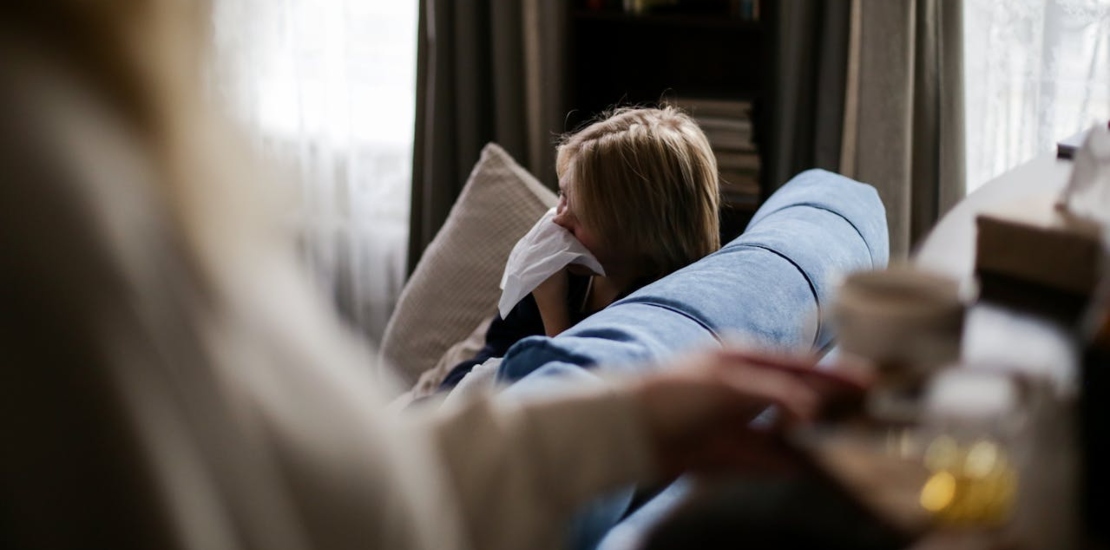 Ребёнок сидит на диване и сморкается.