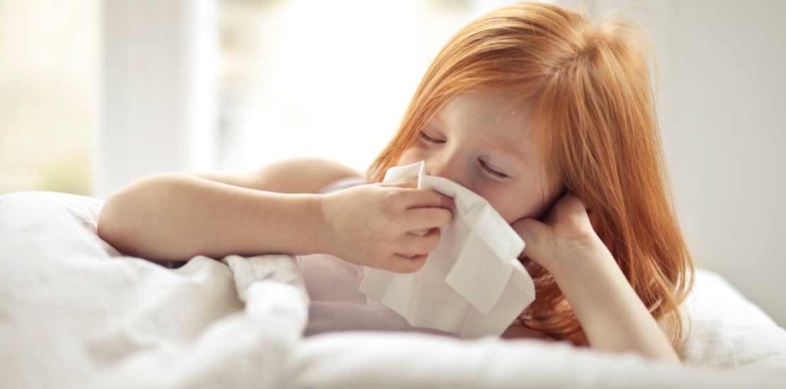 A little girl is lying in bed and blowing her nose.






