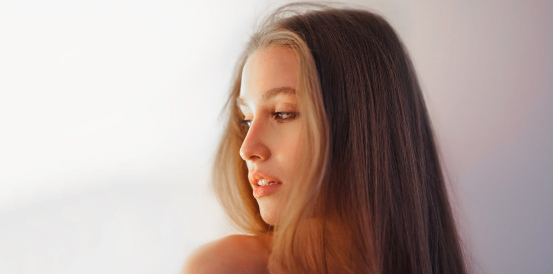 Девушка с длинными волосами проводит пальцами по волосам.