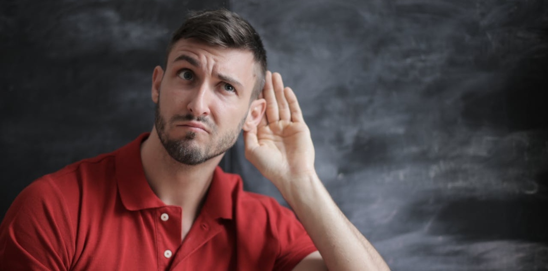 A man is holding his hand to his ear and listening to something.