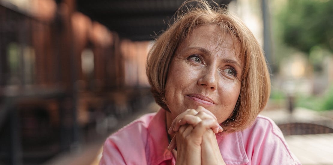 A middle-aged woman sitting outdoors, smiling and looking into the distance