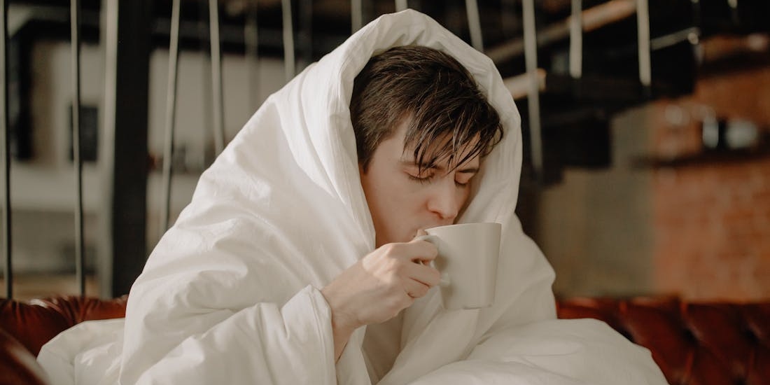 A person under a blanket with a cup of tea during a viral infection that can cause labyrinthitis (Vestibular Neuritis)