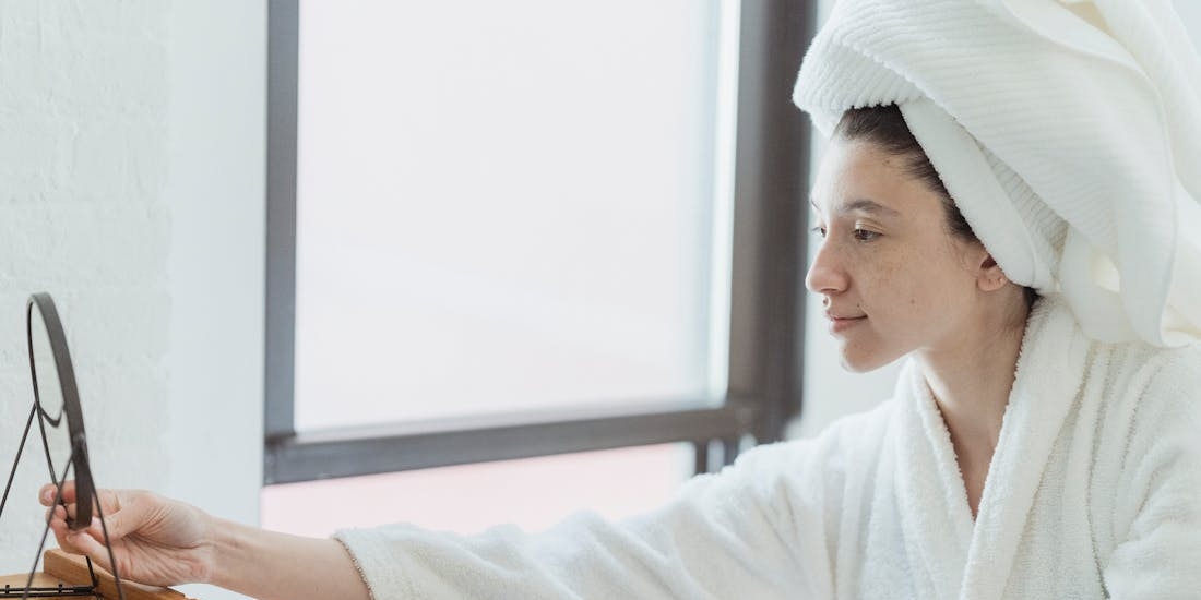 Osoba ispred ogledala nanosi negu, što je svakodnevna rutina koja pomaže pripremiti kožu pre odlaska na letovanje