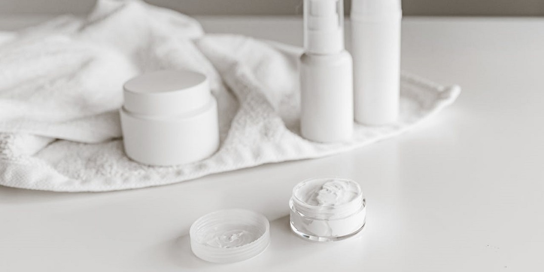 Kolekcija kremi i preparata za negu kože raspoređenih na belom peškiru