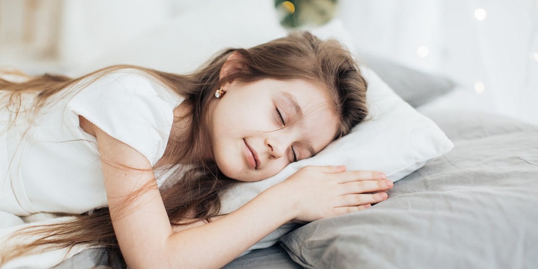 A little girl is sleeping peacefully on a white pillow.