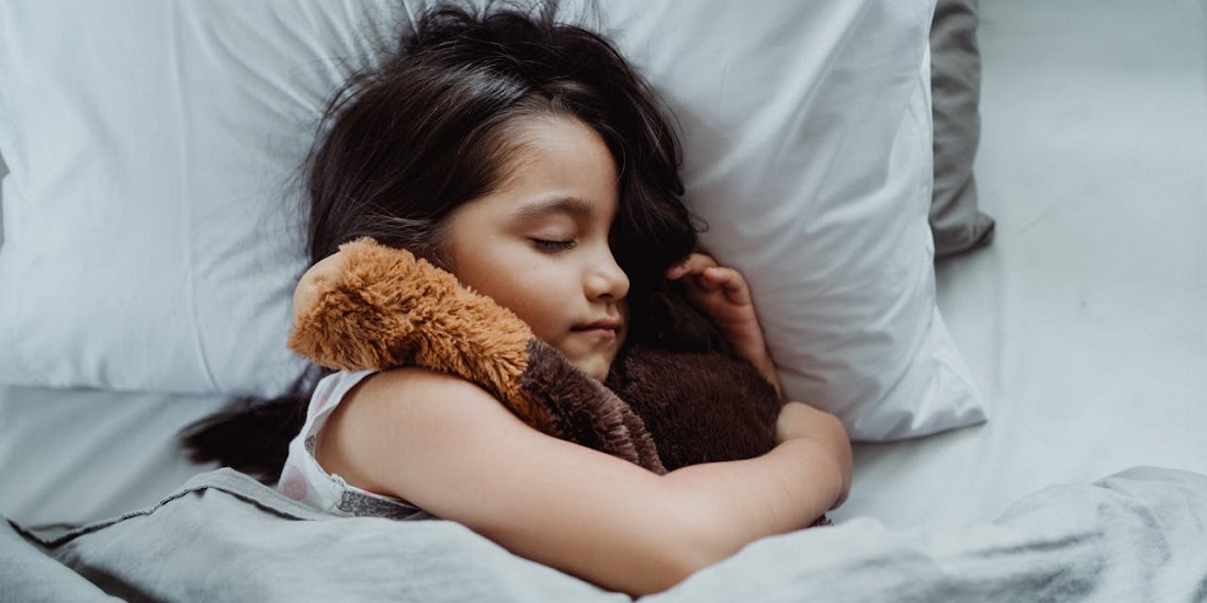 A little girl is sleeping with a stuffed toy in her arms.