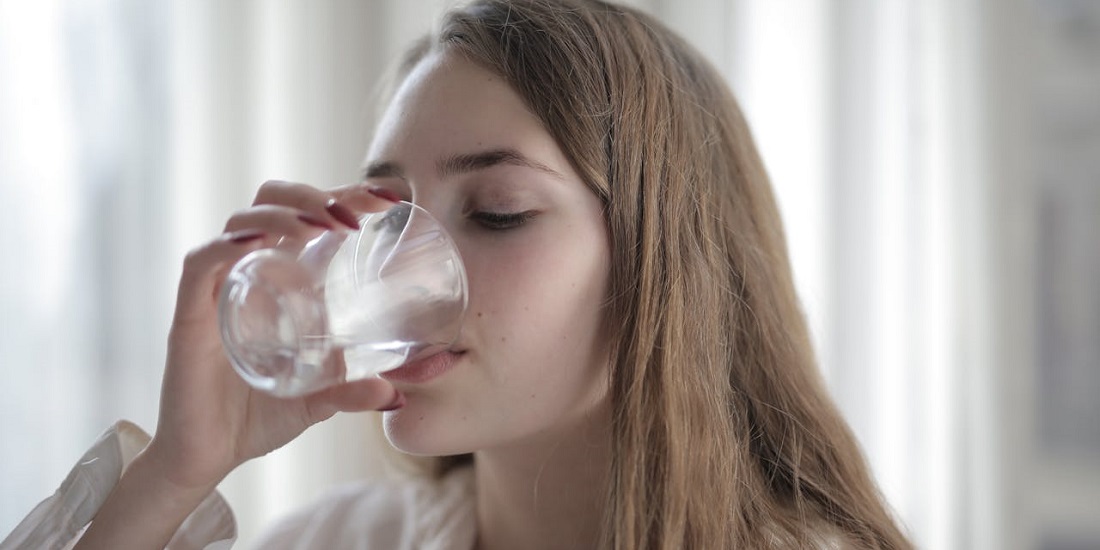 mlada žena pije vodu jer zna da je hidratacija važna dok traje oporavak nakon tretmana plazmom