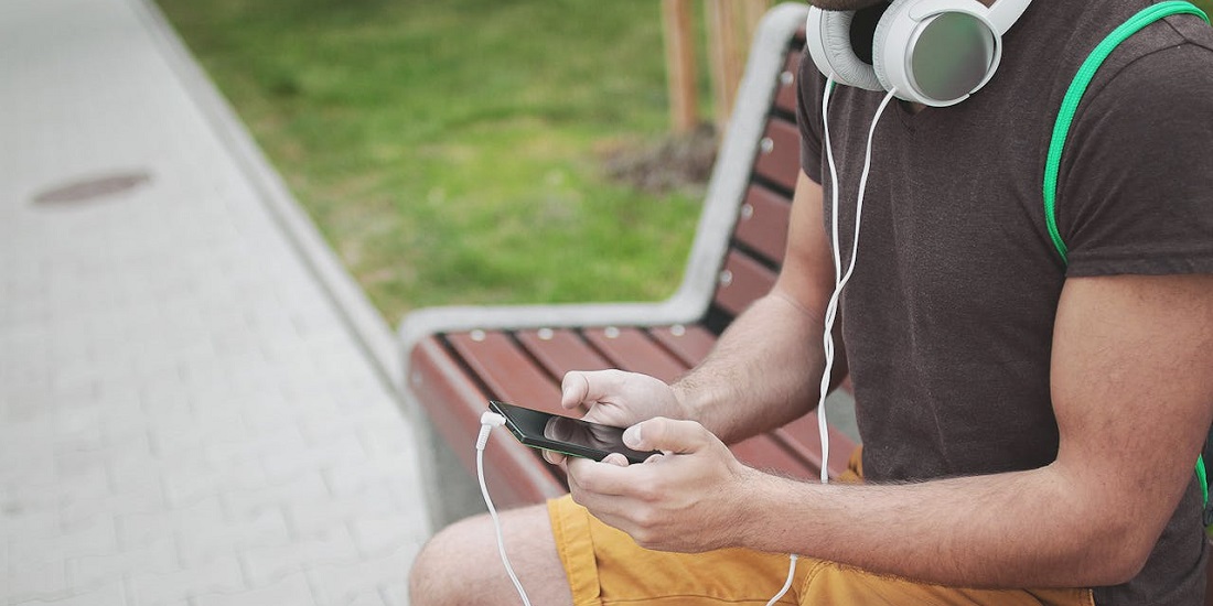 Mladić koristi telefon sa slušalicama na klupi