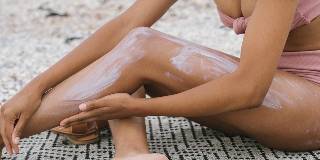 devojka nanosi kremu za zaštitu od sunca na noge