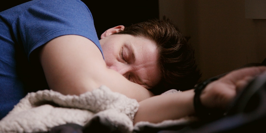 Muškarac spava sklupčan, pokriven mekanim ćebetom.