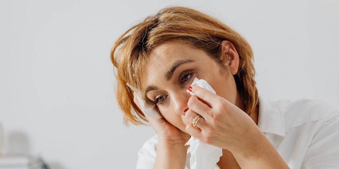 Umorna žena briše suze maramicom kod kuće.