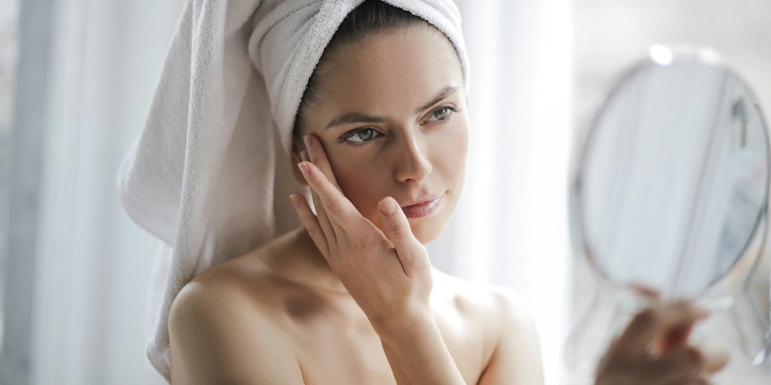 Žena sa peškirom na glavi gleda u ogledalo rezultate koje daje skinimalizam pristup