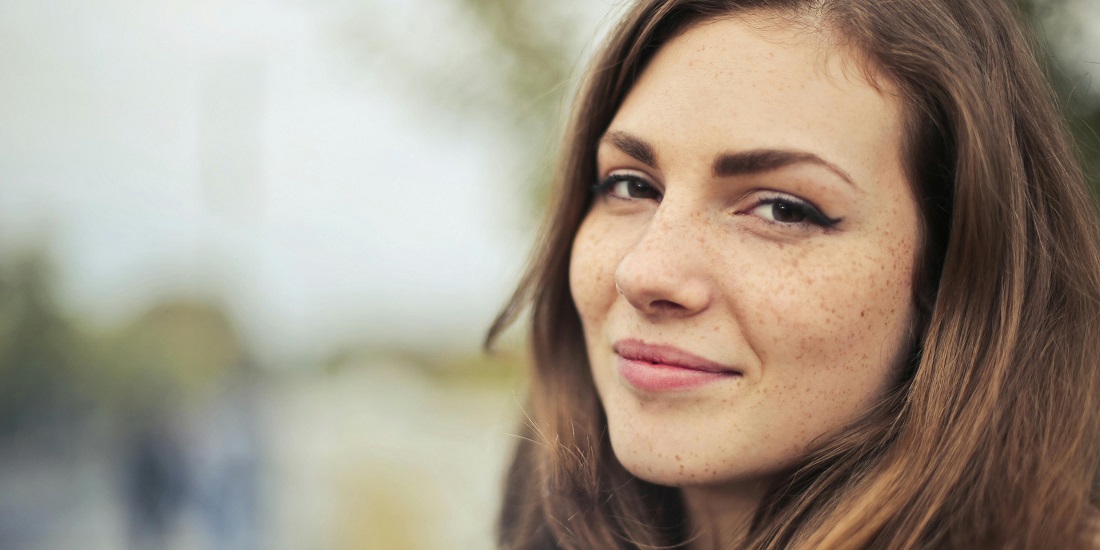 Žena sa pegama osmehuje se u prirodnom svetlu.