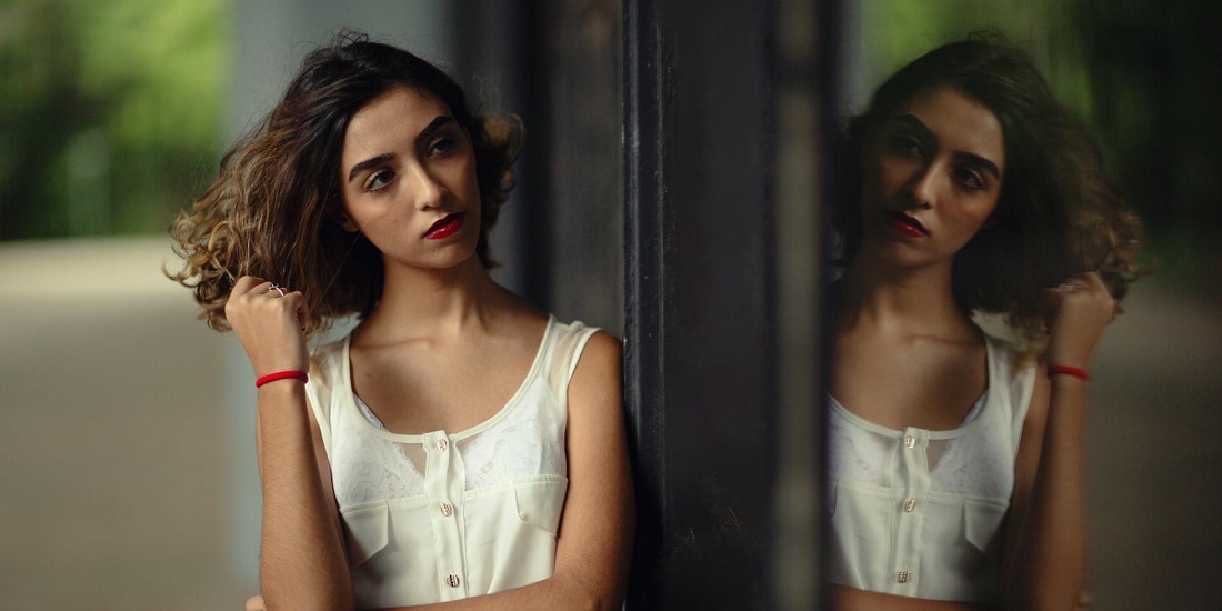 A young woman looks at her reflection and thinks about skin care.