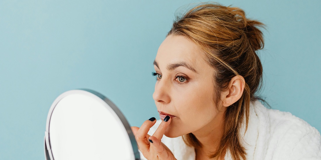 Žena nanosi balzam na suve i ispucale usne pred ogledalom.