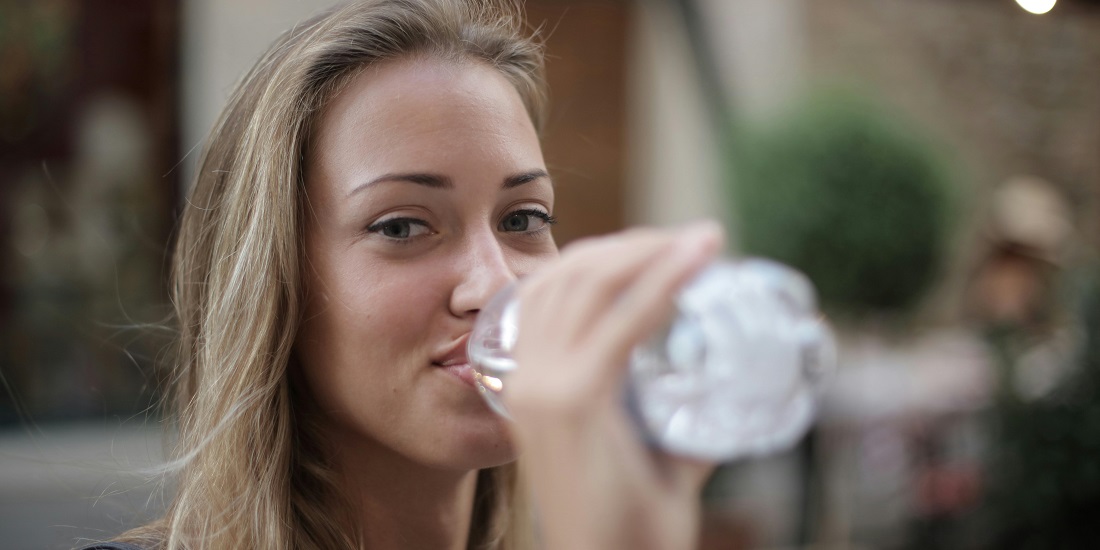 A woman drinks water and takes care of skin hydration.