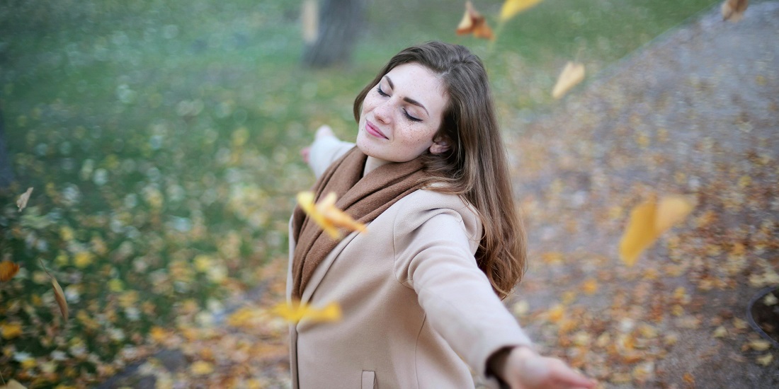 A girl in a coat enjoys the falling leaves because she knows how you protect your skin from the wind