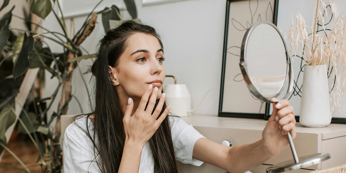 Žena posmatra lice u ogledalu i proverava kako koža reaguje na manjak sunca i vitamina D
