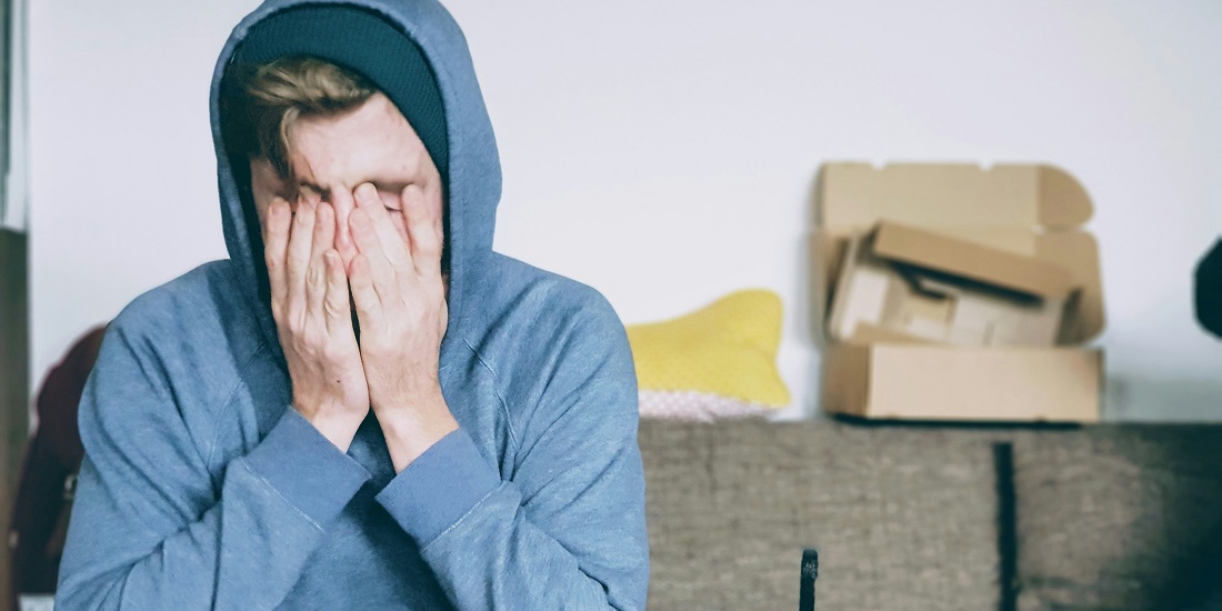 A man in a blue shirt feels somatic stress symptoms appearing and holds his nose.