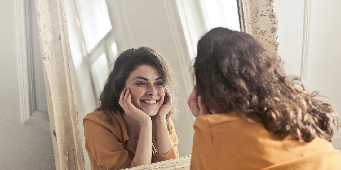 Zadovoljna žena posle estetskih tretmana, nasmejana ispred ogledala.