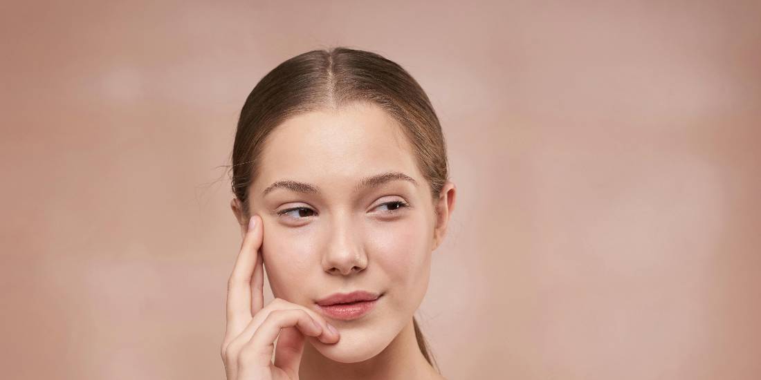 A woman touches her cheek, thinking about skin care.