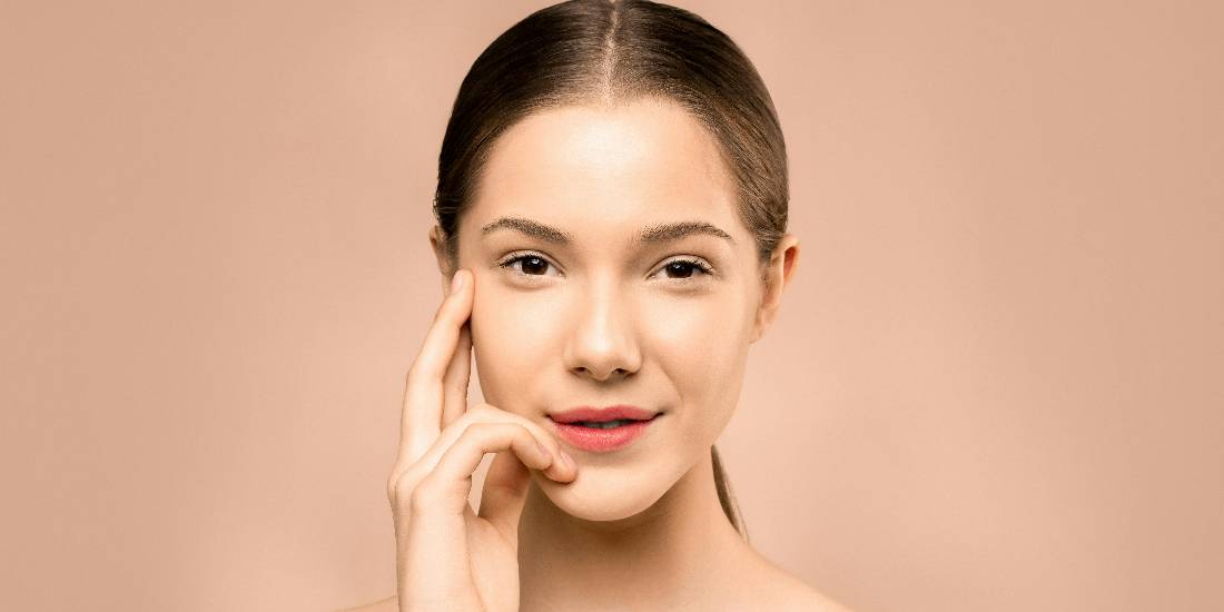 A young woman touches her face.