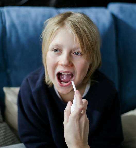 The child is spraying medicine on their throat