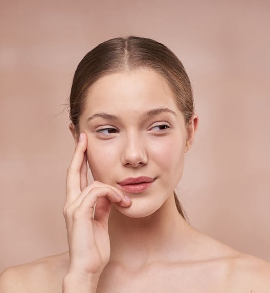 Mlada žena sa čistom, blistavom kožom, dodiruje lice i gleda u stranu