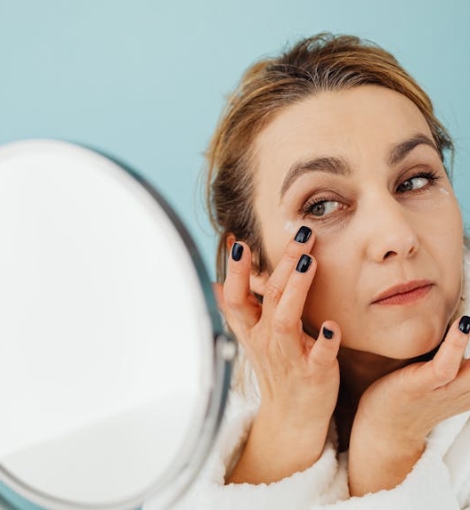 Žena gleda u ogledalo i nanosi kremu čini da koža lica u menopauzi izgleda negovano