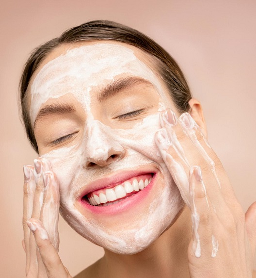 Žena sa širokim osmehom pere lice penom za čišćenje