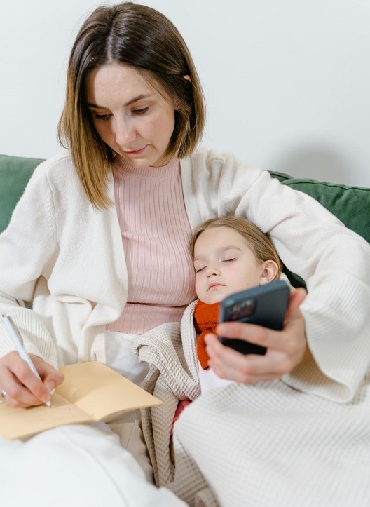 Mama drži ćerku dok piše i koristi telefon.