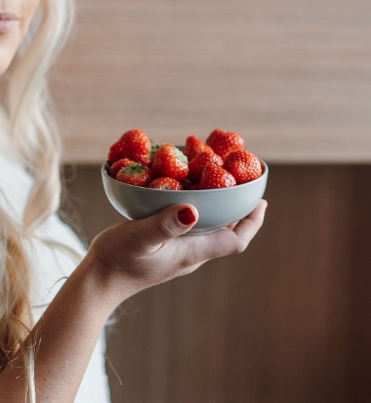 Žena drži činiju svežih jagoda u ruci