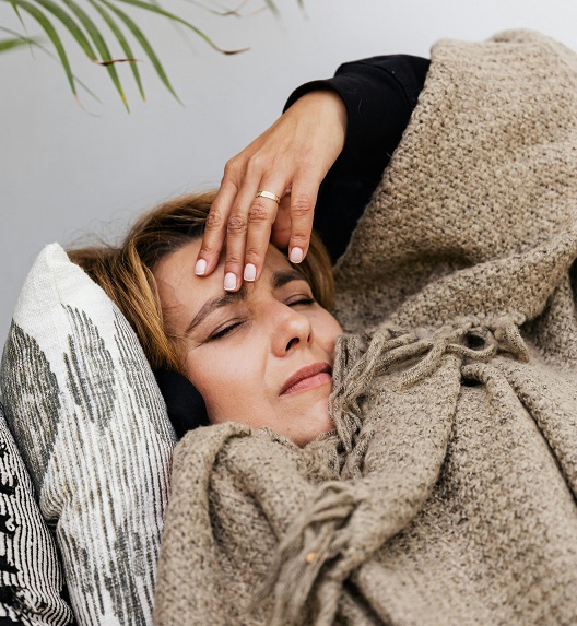 Žena leži i drži čelo zbog bola.