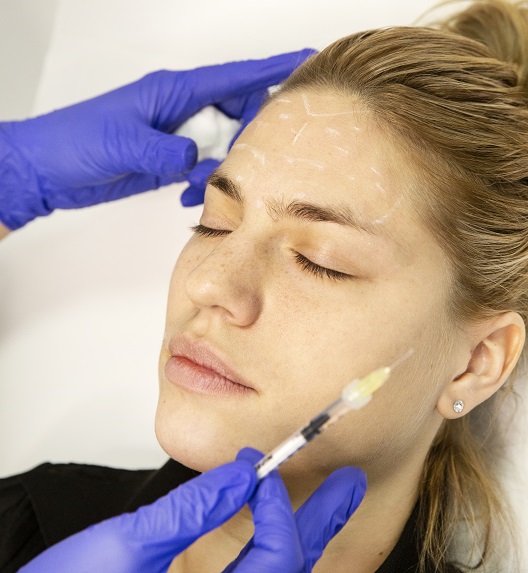 Pacijentkinja zatvorenih očiju prima injekciju u lice.