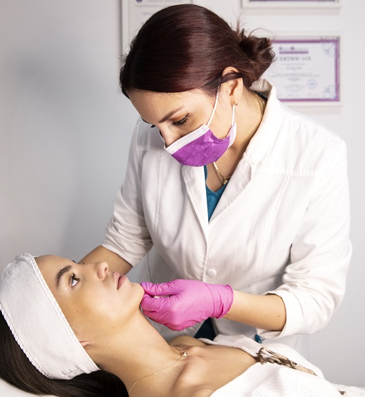 Doktorka pregleda kožu lica pre tretmani za nazolabijalne bore.