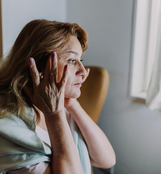 A middle-aged woman applies face cream while massaging her face