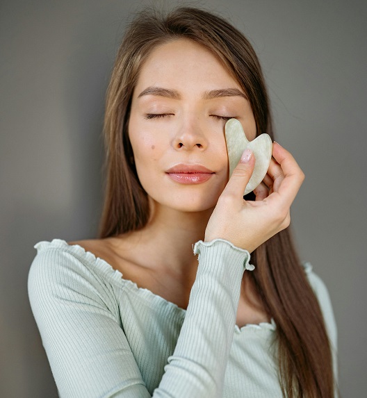 A woman uses a gua sha tool for her face.